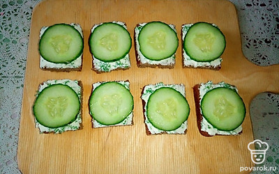 Нарежьте огурец кружочками толщиной 3-4 миллиметра и выложите по одному кружочку на квадратики бородинского хлеба с творожным сыром и укропом.