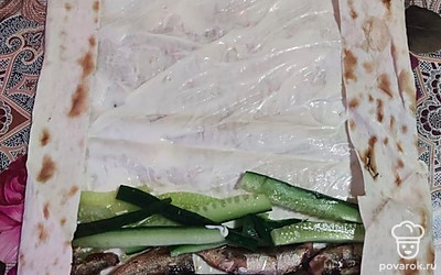 Смажьте весь лаваш соусом. Вниз выложите шпроты (целиком), чуть выше — огурец.