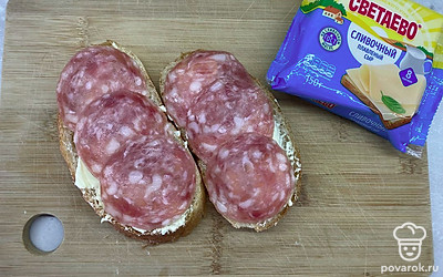 Поверх сливочного масла положить ломтики колбасы.