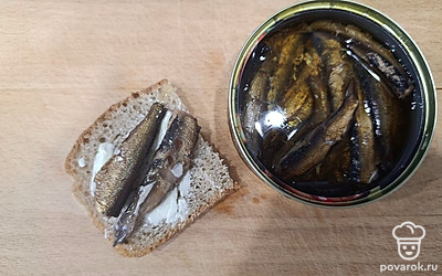 Выложите на хлебные ломтики шпроты с маслом.