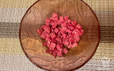 Отрежьте пару ломтиков сырокопченой колбасы, очистите от кожуры, нарежьте в салатник кубиками.