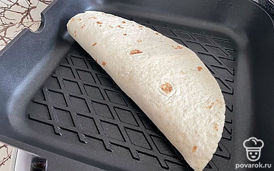 Сверните тортилью пополам. Разогрейте сухую сковородку и выложите на нее лепешку.