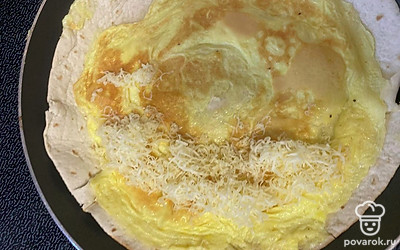 Как омлет обжарится, перевернуть и посыпать на одну половину тертый сыр.