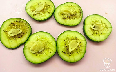 На огурце сделайте надрезы, натрите солью и перцем, сверху выложите дольки чеснока.