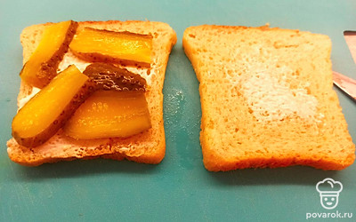 Хлеб для тостов намажьте сметаной, сверху выложите нарезанные тонкими ломтиками корнишоны.