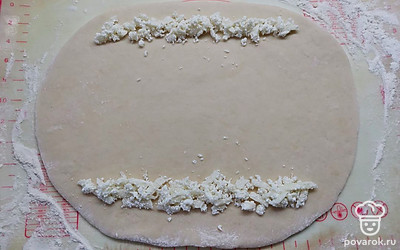 Кусок теста раскатать в овал толщиной примерно 7 миллиметров. Вдоль длинных сторон выложить полосочки отложенной сырной смеси. 