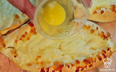 Достаньте лодочки из духовки, примните сыр и вылейте в середину сырое яйцо, затем поместите хачапури в духовку еще на 3 минуты.