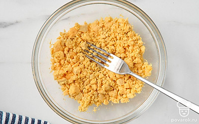 Остудите яйца в холодной воде и очистите от скорлупы. Разрежьте яйца вдоль пополам, удалите из них желтки и переложите их в миску. Разомните желтки вилкой.