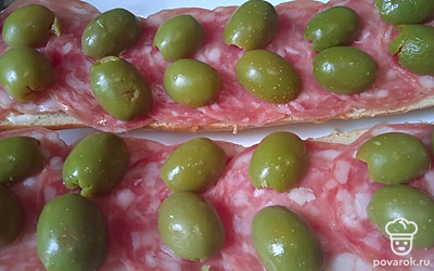 Оливки разрежьте пополам. Разложите на колбасе.