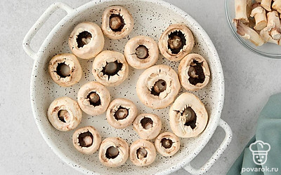 Аккуратно удалите грибные ножки, чтобы не повредить шляпки. Положите шляпки углублением вверх. Уложите грибы в форму для запекания.