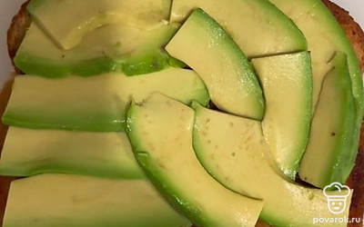 Сначала нарежьте помидоры, лук и огурцы на тонкие кружочки. Затем разрежьте авокадо пополам, удалите косточку и выньте мякоть ложкой. Разрежьте на слайсы авокадо и положите на хлеб.