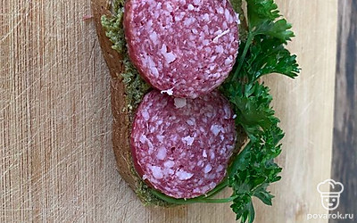 Намажьте на подсушенный хлеб соус песто, положите салями, украсьте петрушкой.