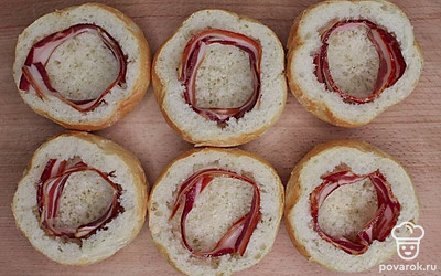 Уложите по кругу внутрь ломтики бекона, по две штуки на каждую. Разбейте в середину по куриному яйцу.