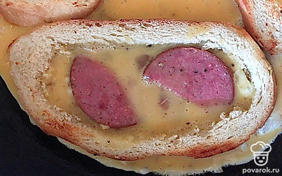 Вылейте на колбасу яичную смесь, заполнив «рамку» из хлеба, посолите и поперчите. Обжарьте мякиши и выложите их на яйцо. Убавьте огонь и жарьте до готовности яйца.