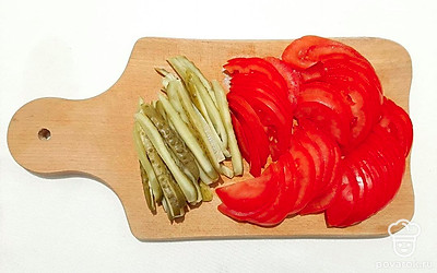 Нарежьте маринованные огурцы тонкой соломкой. Помидоры – кружочками, которые затем нужно разрезать пополам.