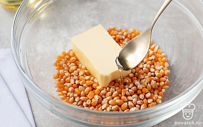 Выложите кукурузные зерна в глубокую емкость для микроволновой печи. Добавьте к ним растительное и сливочное масло. Все хорошо перемешайте.