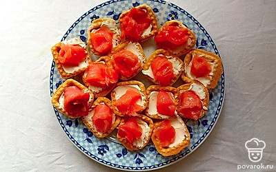 Рыбу нарежьте тонкими ломтиками. Аккуратно скрутите полоски розочками и уложите на сыр, слегка вдавливая рыбу в творожную массу.