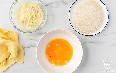 Крупно натрите сыр. Разбейте яйцо в миску, всыпьте к нему соль и перец, хорошо размешайте. Насыпьте панировочные сухари на плоскую тарелку.