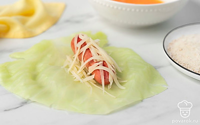 Разложите капустные листья на столе. Поместите по центру листьев по 1 сосиске. Равномерно посыпьте сосиски сыром и плотно сверните капустные листья в рулет. Обмакните заготовки в яйцо и обваляйте их в панировочных сухарях.