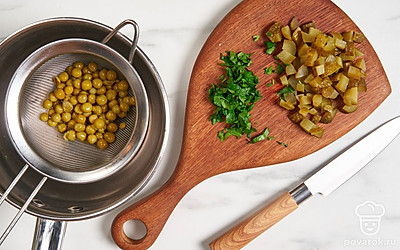 Нарежьте маринованные огурцы мелким кубиком. Измельчите петрушку. Выложите горошек из банки в дуршлаг и дайте лишней жидкости стечь.