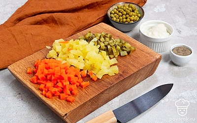 Подготовьте ингредиенты. Очищенный картофель нарежьте средними кубиками, морковь и огурцы — кубиками поменьше. Консервированный горошек переложите в миску, лишнюю жидкость слейте.