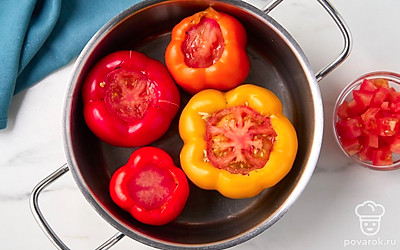 Уложите нафаршированные перцы в сотейник или казан. Нарежьте второй помидор кубиками, положите их в сотейник вокруг перцев.