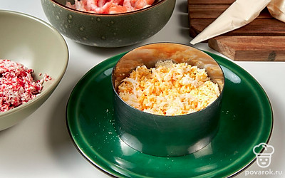 Сформируйте блюдо. Для этого возьмите салатницу, форму с невысокими бортиками или плоское блюдо и формовочное кольцо. Первым слоем натрите на терке с крупными ячейками картофель, сделайте сеточку из майонезного соуса. Далее — сыр и соус. Затем добавьте яйца, натирая их на мелкой терке, нанесите слой соуса. Выложите крабовые палочки и небольшое количество соуса. Разровняйте поверхность и сверху разложите креветки.