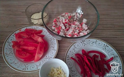 Крабовые палочки нарежьте мелким кубиком. Помидоры нашинкуйте дольками. Перец тоже нарежьте дольками, чеснок измельчите.