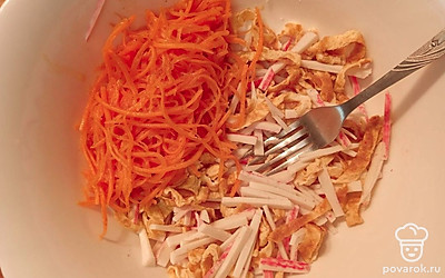 В глубокую тарелку кладем яичные блинчики, крабовые палочки и добавляем корейскую морковь. 