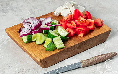 Подготовьте ингредиенты для салата. Порежьте перец, огурцы, помидоры и фету на крупные кубики, а лук — на полукольца. В небольшой миске смешайте растительное масло и бальзамический уксус.