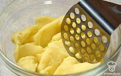 Остудите готовый картофель и очистите от кожуры. Переложите его в миску и измельчите при помощи толкушки. 