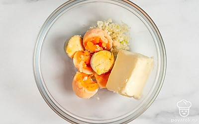 Разрежьте яйца пополам. Достаньте желтки и выложите их в миску. Туда же добавьте измельченный чеснок и сливочное масло. Перемешайте, чтобы получилась однородная масса.