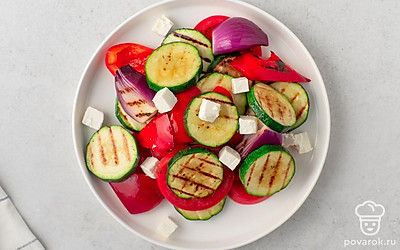 Переложите ломтики обжаренных овощей на сервировочное блюдо. Добавьте к ним кружочки помидоров и кубики сыра фета.