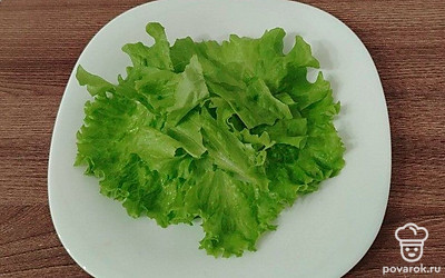 На тарелках разложите салатные листья. Помидоры нарежьте тонкими слайсами. 