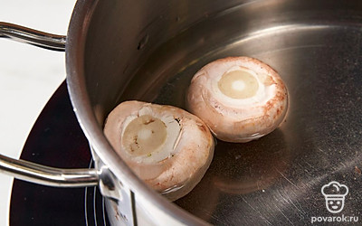 Вскипятите в кастрюле воду. Аккуратно отделите ножки шампиньонов от шляпок. Опустите шляпки в кипящую воду и отварите их в течение 5 минут.