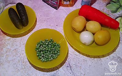 Достаем два соленых огурца. Размораживаем зеленый горошек, промыв его под горячей водой. Чистим лук, три сваренных картошки и морковь. 
